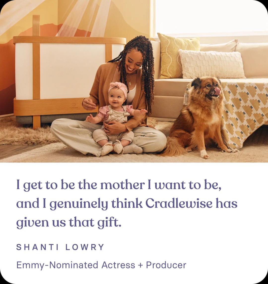 Shanti Lowry, who's an Emmy Nominated Actress + Producer and a satisfied Cradlewise customer, smiling as she holds her baby next to the Cradlewise smart crib, highlighting her positive review and experience with the crib’s features and benefits.